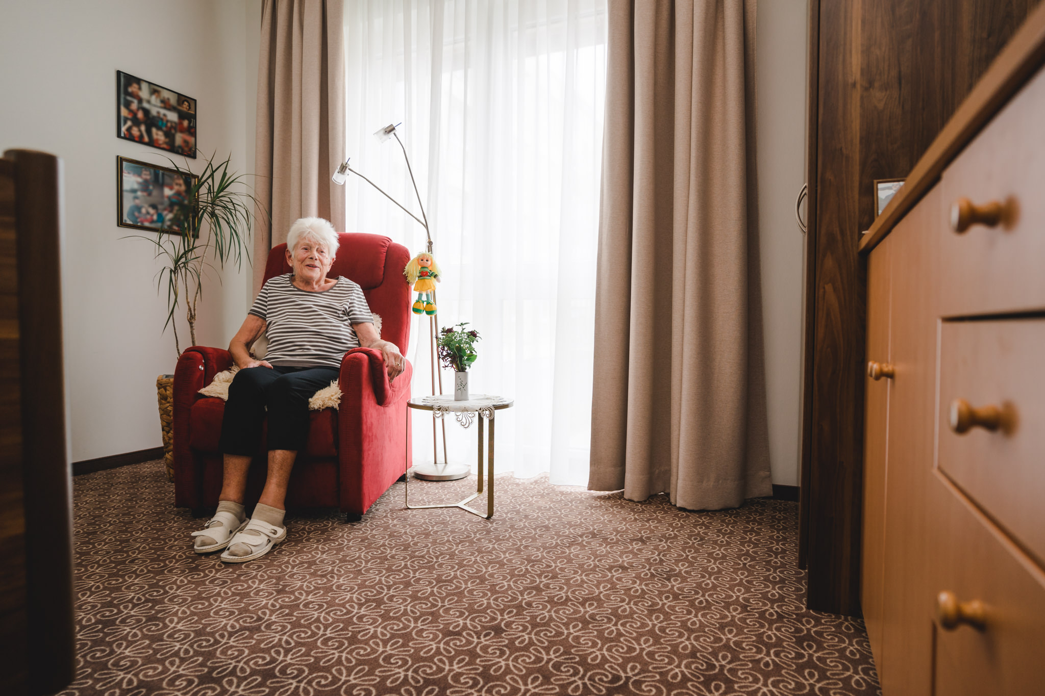 ältere Bewohnerin sitzt in ihrem Zimmer auf Sessel